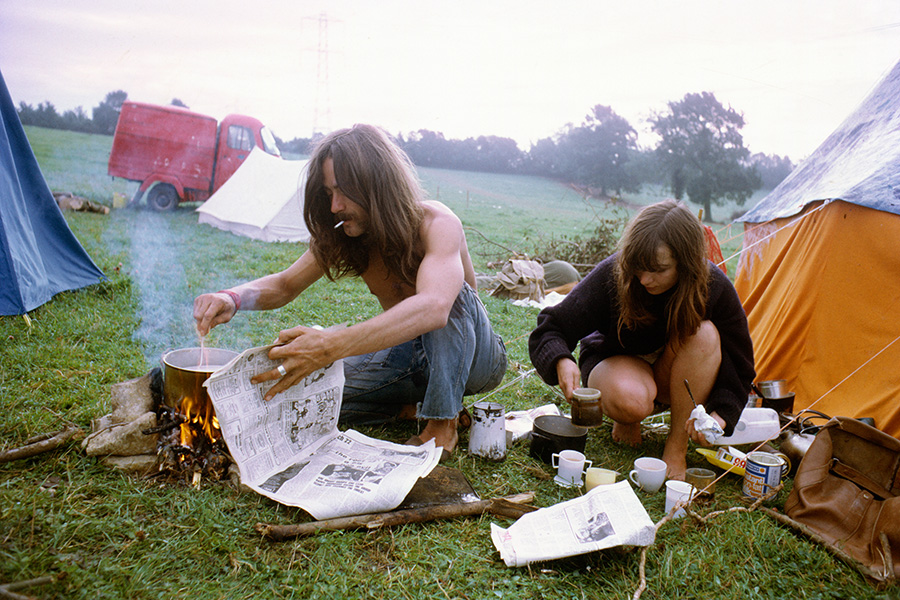At the first Glastonbury Festival in September 1970, a young hippy couple prepares food on a campfire by their tent.